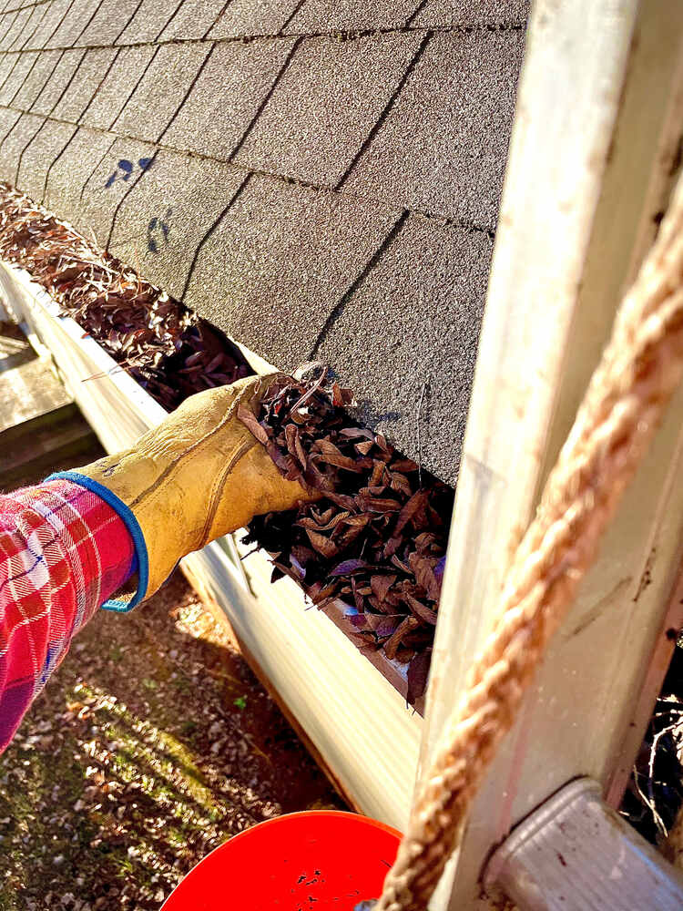 professional with yellow glove cleaning out gutter on home