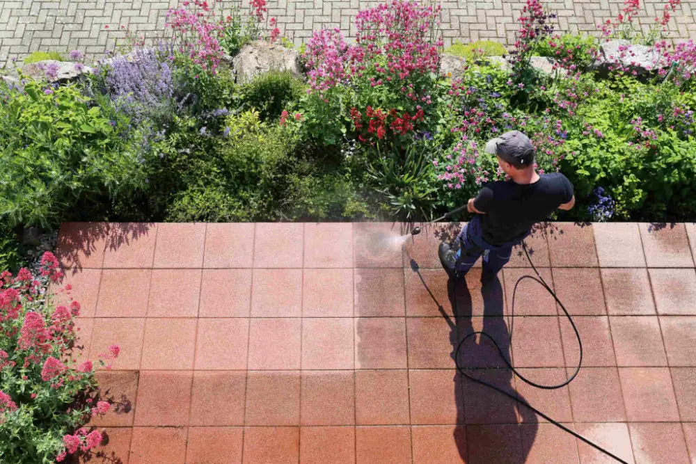 Worker pressure washing outdoor tiles, removing built-up dirt and grime for a fresh and vibrant patio surface.